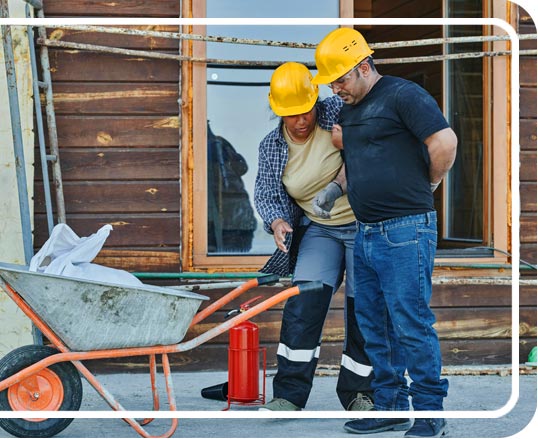A female worker helping a male worker with a back injury on a construction site