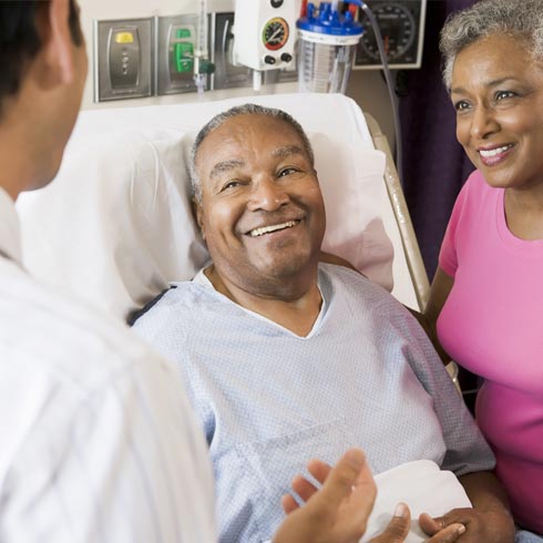 Man in hospital bed speaking to a doctor with a smile on his face.