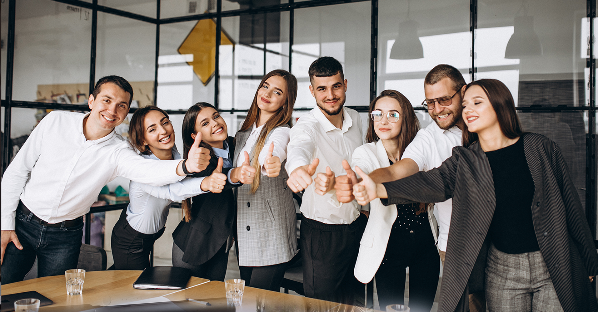 Group of office workers leaning in together giving a thumbs up
