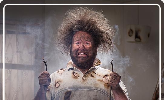 A comical picture of a man with singed clothing and hair holding 2 frayed electrical wires