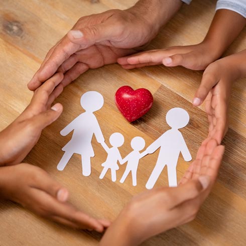 several sets of hands wrapping around a paper cut out of a family in a protective circle with a heart in the middle
