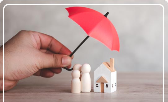 A hand holding a red umbrella over a wooden figures of a family next to a house