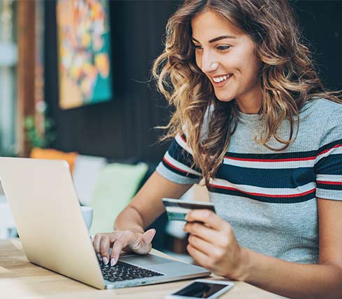 Smiling woman holding credit card looking at a computer screen