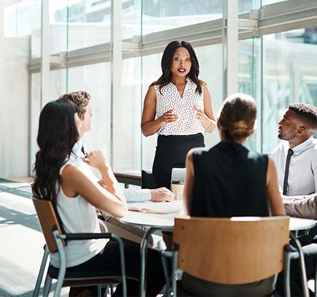 A female corporate executive talking to a group of other corporate executives